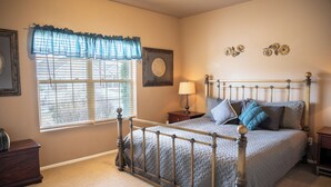 A bedroom with a metal bed frame, a window with blinds, a bedside table with a lamp, and a dresser. - COMFY  2 bedroom 1 bath, living room, mini kitchen with 70" smart TV & Grill (Montrose)