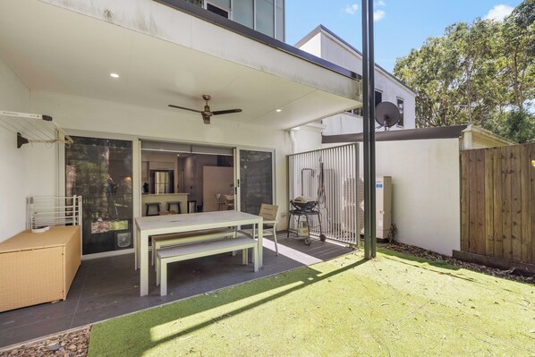 A modern outdoor patio with a dining table and chairs, a ceiling fan, and a wooden fence.
