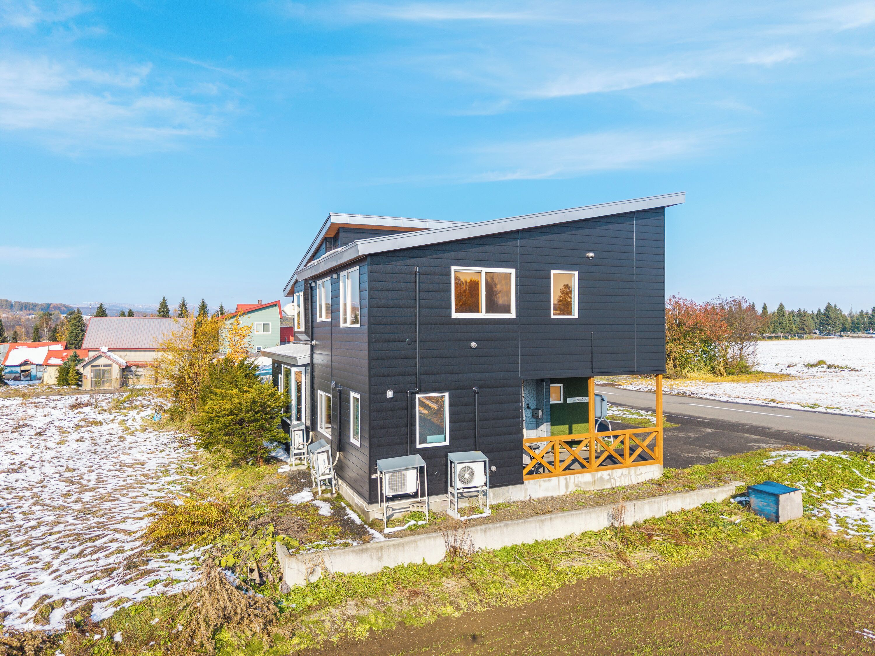 A two-story building with a balcony, outdoor air conditioning units, and a view of a snowy landscape.