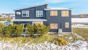 A modern two-story house with a dark exterior, multiple windows, and a visible air conditioning unit. - THE LANDSCAPE (Kamifurano)