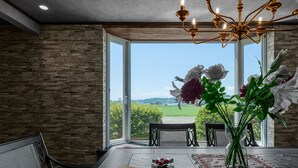 A dining area with a table, chairs, a chandelier, and a view of greenery through large windows. - THE LANDSCAPE (Kamifurano)