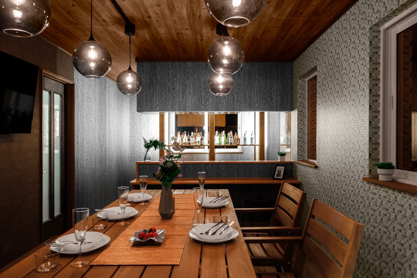Comedor con una larga mesa de madera lista para una comida, zona de bar con botellas y un diseño de techo moderno.