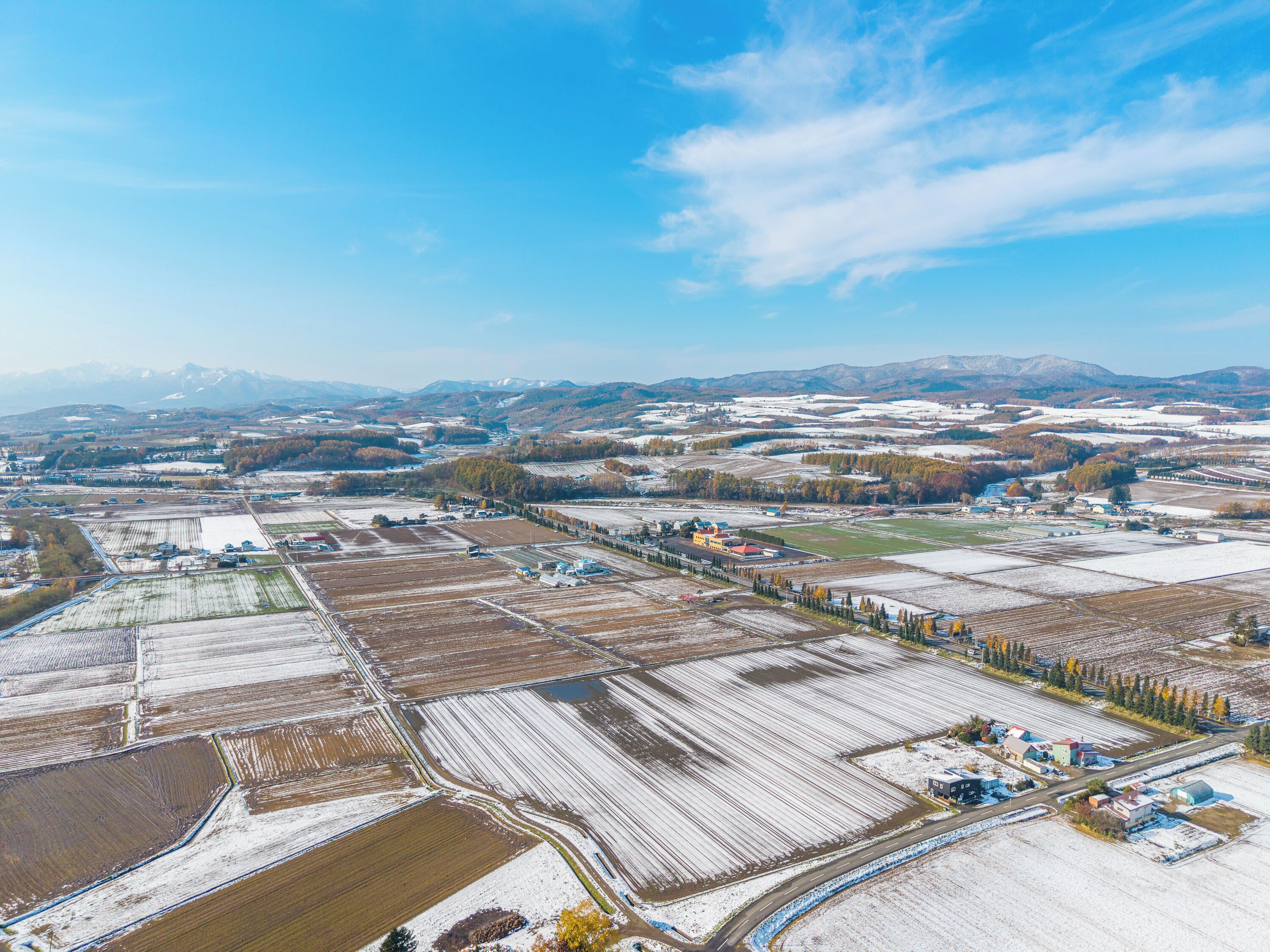 An aerial view of a rural landscape with fields, buildings, and mountains in the distance.