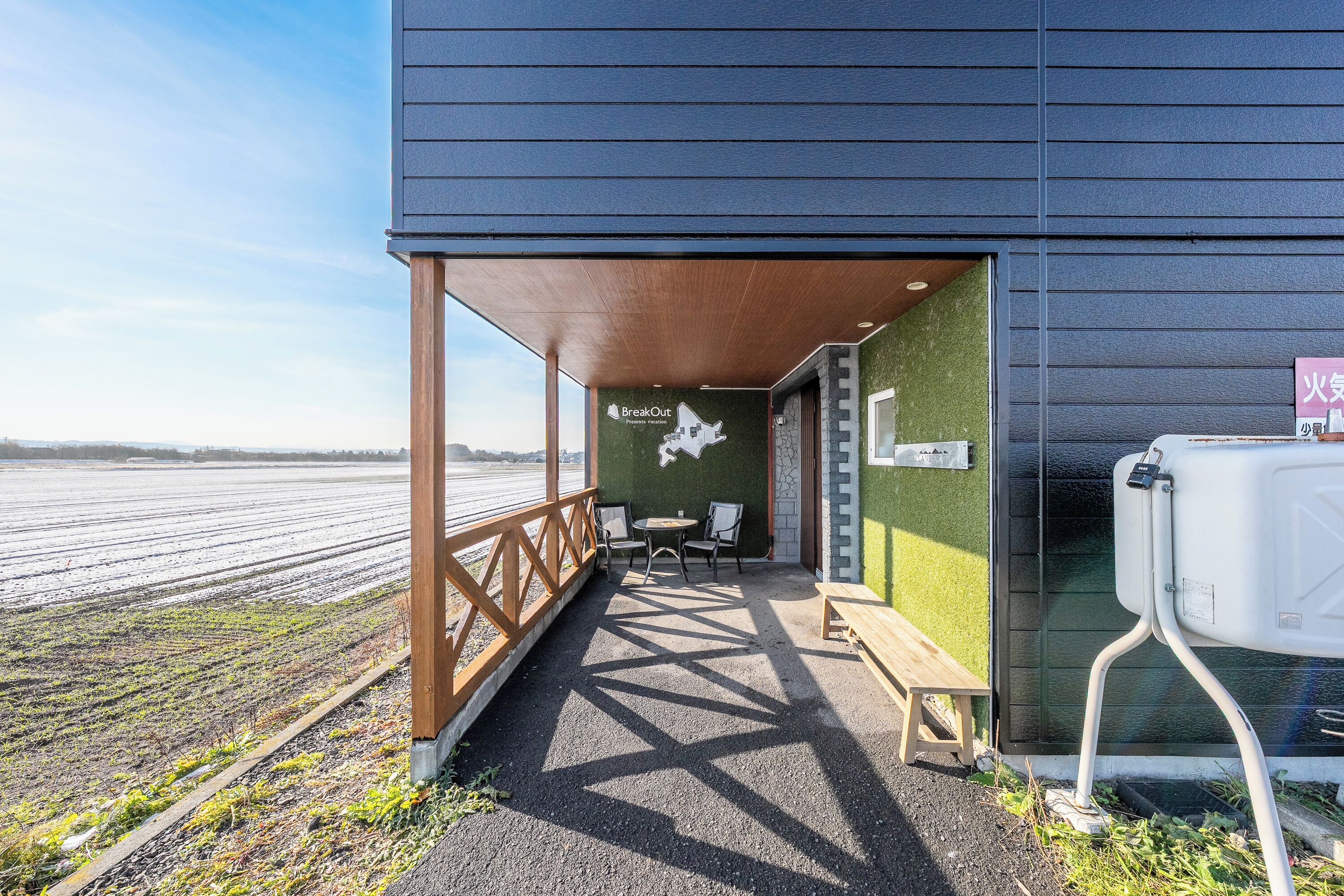 A covered outdoor seating area with a view of a field, a wooden bench, and a sign for 'BreakOut'.