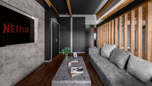 A modern interior with a grey couch, a wooden slatted wall, and a Netflix sign on the wall. - THE LANDSCAPE (Kamifurano)