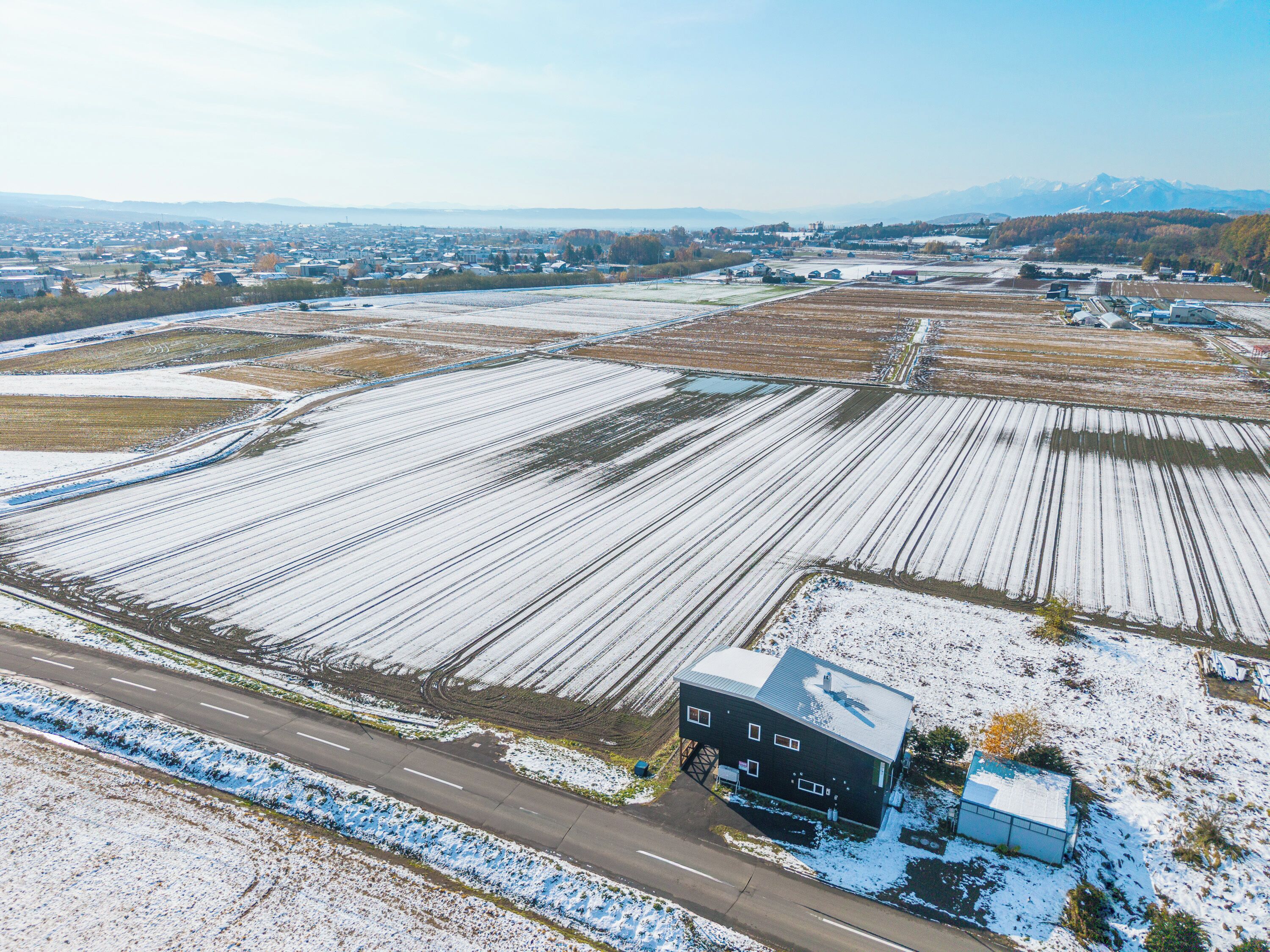 An aerial view of a rural area with snow-covered fields and a single large building with a flat roof.