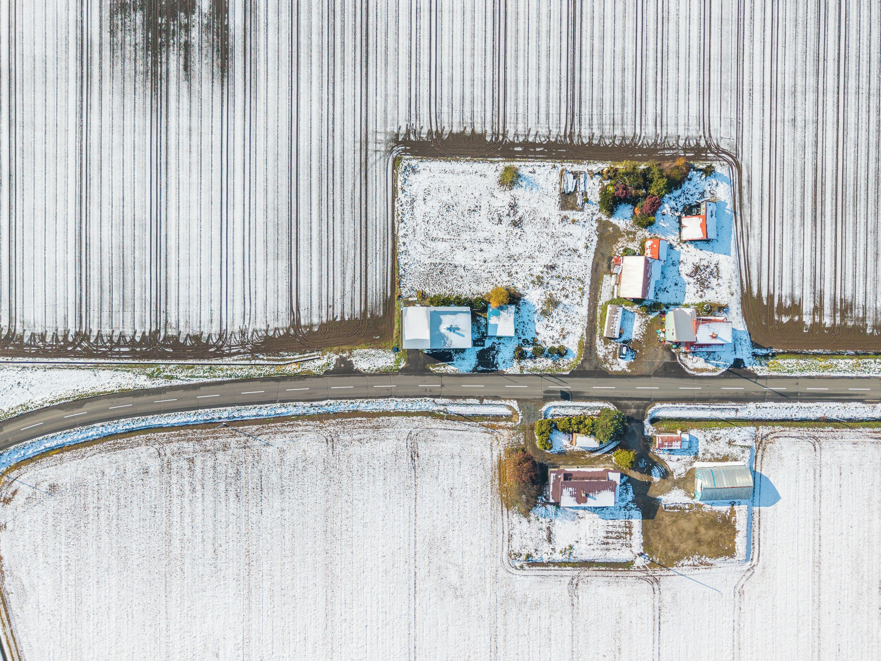An aerial view of a rural area with a road, fields, and several buildings including a large blue structure and smaller buildings.