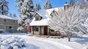 Una casa cubierta de nieve con un porche y una bandera estadounidense.