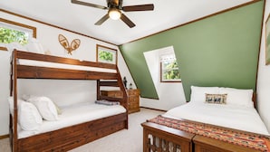 Un dormitorio con una cama litera, una cama individual, un ventilador de techo y una ventana con vistas a la vegetación.