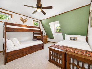 Un dormitorio con una cama litera, una cama individual, un ventilador de techo y una ventana con vistas a la vegetación.