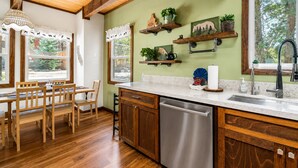 Una cocina con armarios de madera, lavavajillas de acero inoxidable y ventana con vistas a árboles.