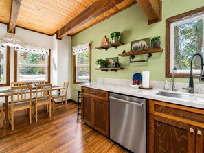 Una cocina con armarios de madera, lavavajillas de acero inoxidable y ventana con vistas a árboles.