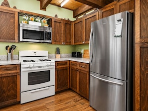 Una cocina con gabinetes de madera, un refrigerador de acero inoxidable, un microondas, una estufa y un tostador.