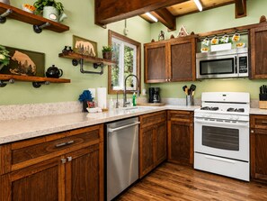 A kitchen with wooden cabinets, a stainless steel dishwasher, a white stove, and a microwave.