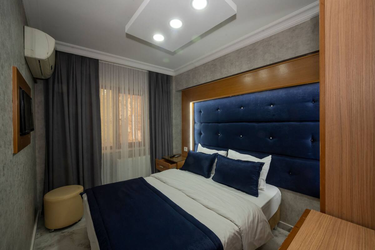 A hotel room with a large bed, a wooden headboard, a bedside table, and a wall-mounted air conditioner.