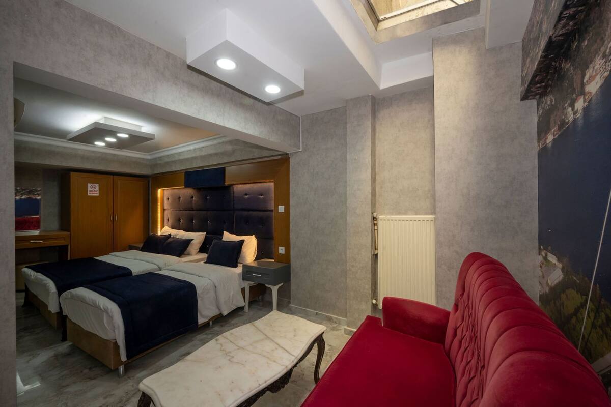 A hotel room with a bed, a red sofa, a small table, and a radiator.