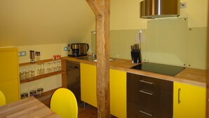 A kitchen with yellow cabinets, a stainless steel coffee maker, and a wooden ceiling beam. - Apartment "summer" - Apartments Baltic - Kate (Schmatzin)