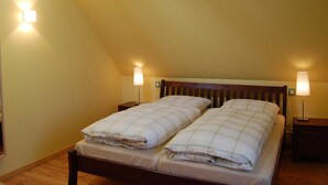 A bedroom with a sloped ceiling, two bedside lamps, a wooden headboard, and a bed with two pillows. - Apartment "summer" - Apartments Baltic - Kate (Schmatzin)