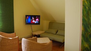 A cozy room with a television mounted on the wall, a green sofa, wicker chairs, and a small table. - Apartment "summer" - Apartments Baltic - Kate (Schmatzin)