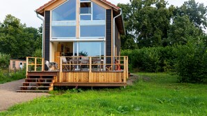 Een houten chalet met twee verdiepingen, een balkon, grote ramen en een houten terras.
