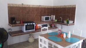Une cuisine compacte équipée d’une cuisinière, d’un four à micro-ondes et d’un évier, avec des carreaux marron et des meubles blancs.