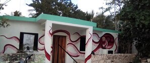 Un bâtiment à deux étages surmonté d’un toit végétalisé, avec une moto garée devant et une fresque représentant des poulpes sur les murs extérieurs.