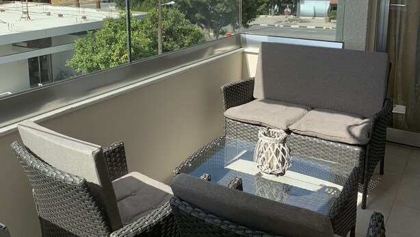 A balcony with wicker furniture and a glass table, overlooking a cityscape with buildings and a church. - Spacious Boutique Apartment (Larnaca)