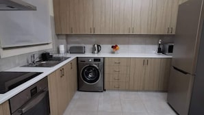 A modern kitchen with light wood cabinets, a stainless steel sink, a built-in washing machine, and a refrigerator. - Spacious Boutique Apartment (Larnaca)