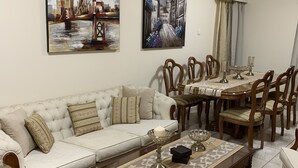 A living room with a sofa, dining table, chairs, and two paintings on the wall. - Spacious Boutique Apartment (Larnaca)