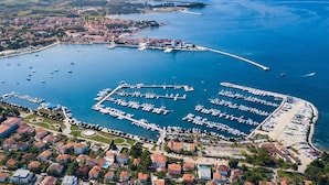 An aerial view of a coastal marina with multiple docks and boats, surrounded by residential buildings and a distant cityscape. - Villa Toscana by Interhome (Umag)