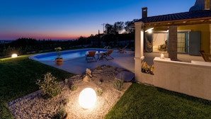 A poolside area with lounge chairs, a pergola, and a stone wall with a fire pit. - Villa Toscana by Interhome (Umag)