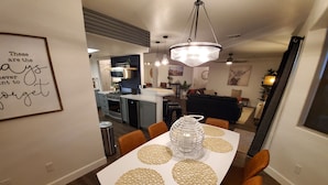 Uma zona de refeições moderna com uma mesa branca, cadeiras laranja e jogos americanos decorativos.