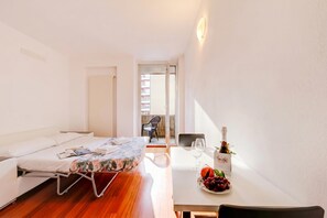 Quarto de hotel com cama, uma mesa de jantar com garrafa de vinho e frutas, e vista para o exterior.