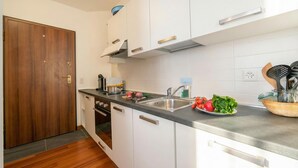Una cocina compacta con armarios blancos, un lavamanos de acero inoxidable y una puerta de madera.