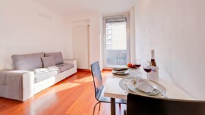 Una sala moderna con sofá, mesa de comedor y vista por una ventana.