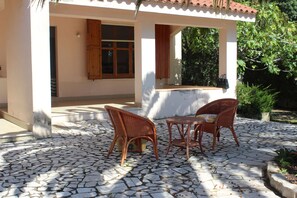 A covered outdoor seating area with two wicker chairs and a small table, surrounded by a stone-tiled patio. - House (S'ena e Sa Chitta   (farz Siniscola))