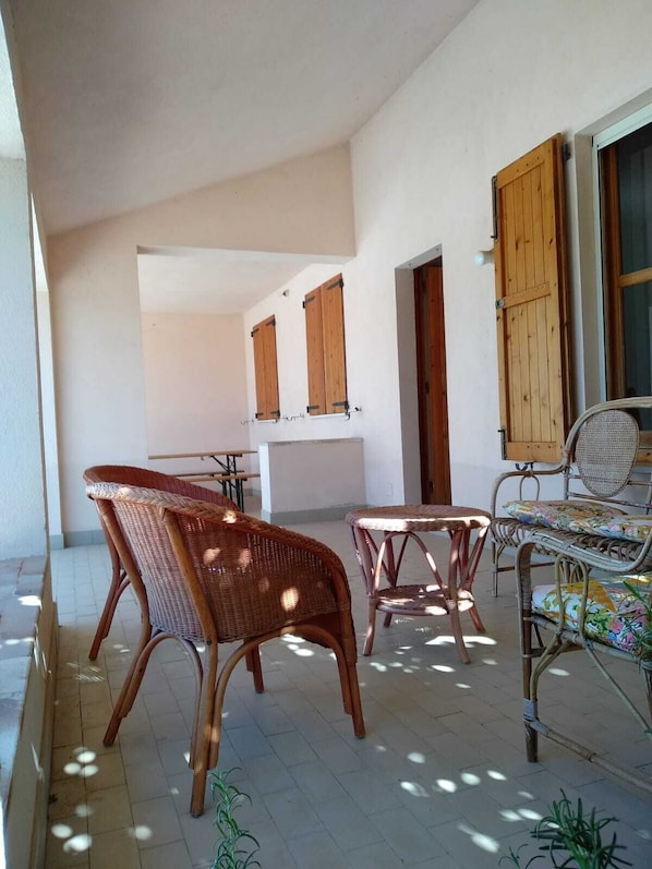 A spacious patio area with wicker furniture, including two chairs and a table, and a wooden door.