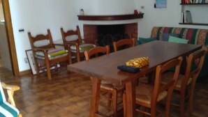 Un coin repas avec une longue table en bois et des chaises, une cheminée et une bibliothèque remplie de livres.