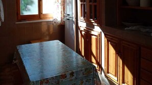 Une cuisine avec des meubles de rangement en bois, un réfrigérateur et une table recouverte d’une nappe à motifs floraux.