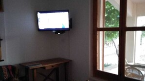 Une pièce avec un téléviseur fixé au mur, une table en bois et une fenêtre donnant sur l’extérieur.
