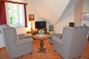 A cozy living room with two armchairs, a small round table, a television, and a window with curtains.