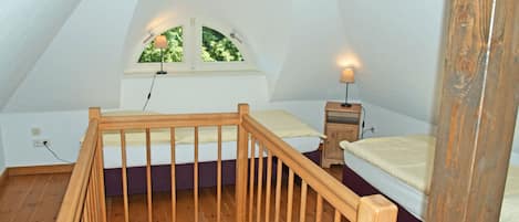 A bedroom with a wooden staircase, a window with a view of trees, a bedside table with a lamp, and a bed with a headboard.