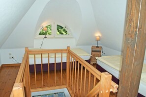 A bedroom with a wooden staircase, a window with a view of trees, a bedside table with a lamp, and a bed with a headboard. - 07 Vacation apartment - Karolas Landhus under the thatched roof (Mönchgut)