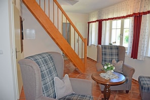 A living room with two plaid armchairs, a wooden staircase, and a small round table with a vase of flowers.