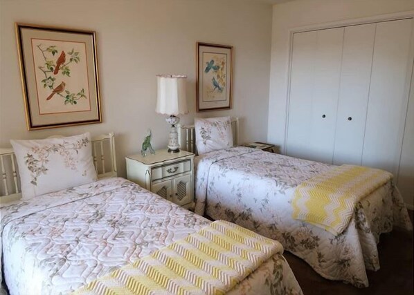 A room with two beds, a nightstand, a lamp, and a wardrobe.