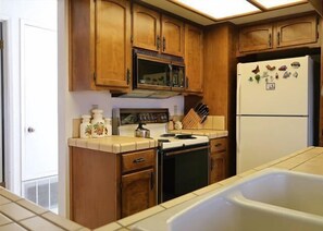 A kitchen with wooden cabinets, a microwave, stove, refrigerator, and a sink.