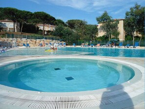 Una grande piscina all'aperto con una sezione circolare, circondata da lettini e ombrelloni.