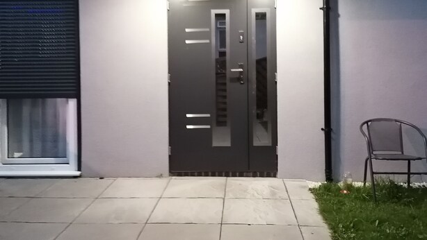 A modern building with a dark-colored entrance door, a small covered porch area with lights, and a chair outside. - Charming 1-bed Apartment in Coventry (Coventry)