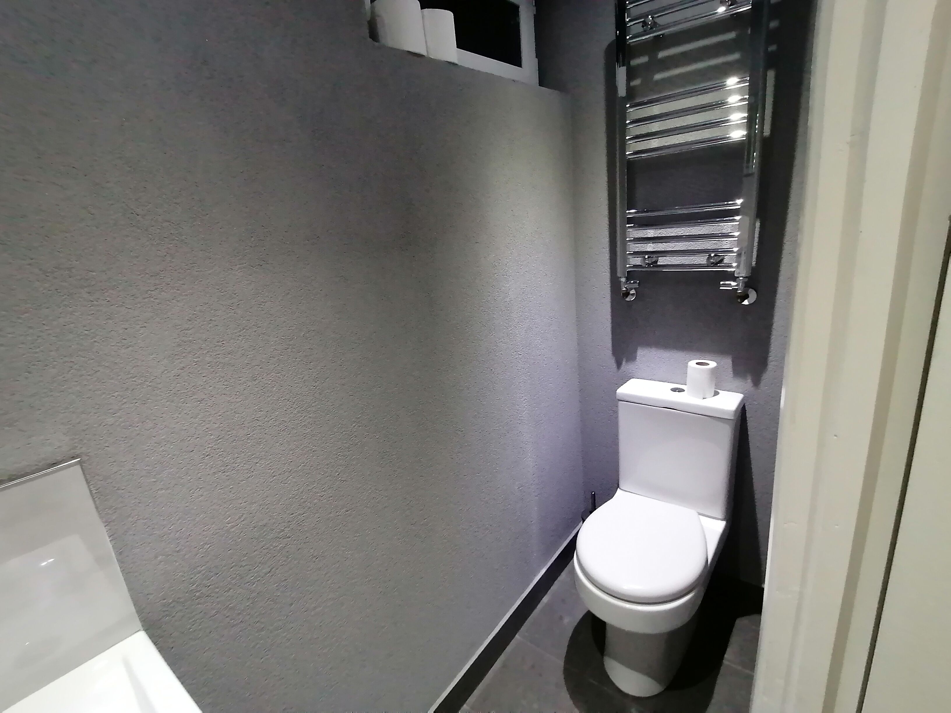 Une petite salle de bain moderne équipée de toilettes, d’un porte-serviettes et d’un support à papier toilette.