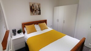 A bedroom with a bed, a nightstand, a bedside table, a wardrobe, and a painting on the wall. - Charming 1-bed Apartment in Coventry (Coventry)